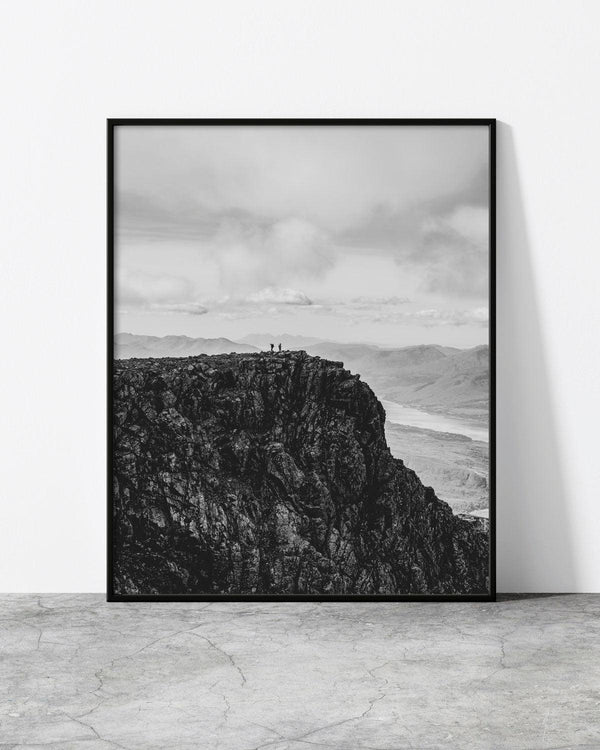 Black and white mountain landscape print featuring two hikers standing on a rugged cliff edge with vast scenery.