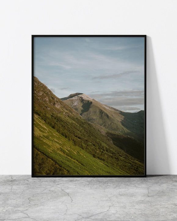 Minimalist landscape print featuring a lush green mountain slope leading to a rugged peak under a soft sky.