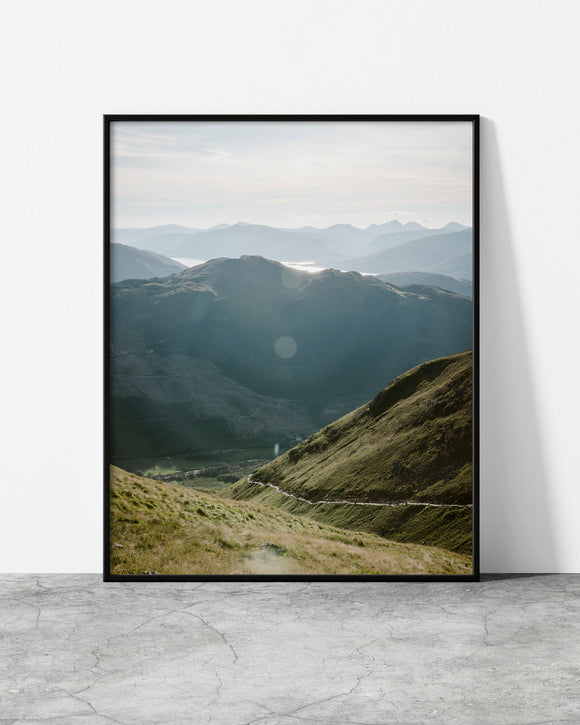 Serene mountain wall art capturing misty peaks and sunlit grassy slopes in a tranquil atmosphere.