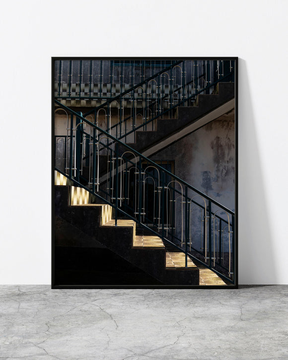 Staircase wall art of teal zig-zag railings and a shaft of light on a weathered concrete stairwell