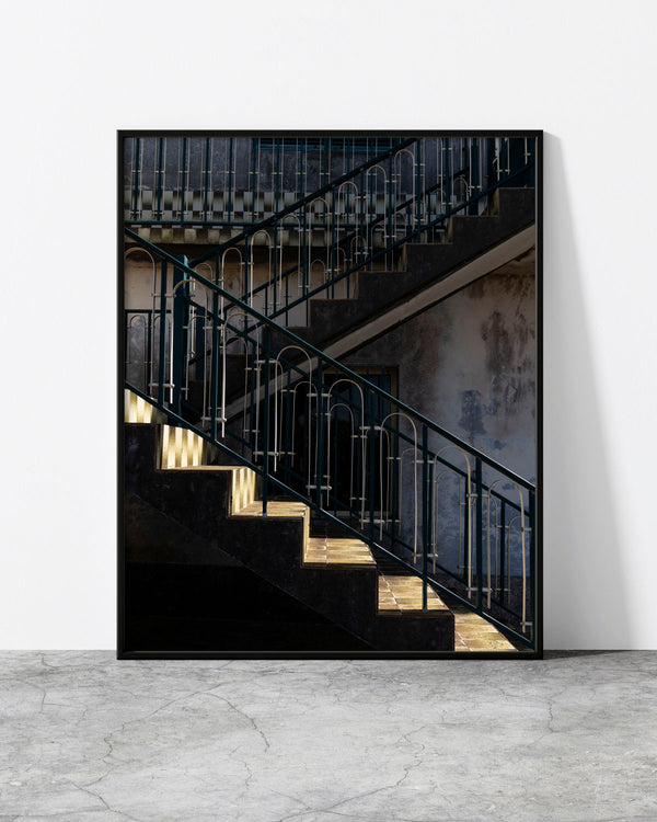 Staircase wall art of teal zig-zag railings and a shaft of light on a weathered concrete stairwell