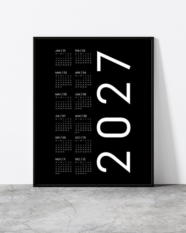 2027 V7 wall calendar with white monthly grids and large vertical year numerals on black, in a black frame.