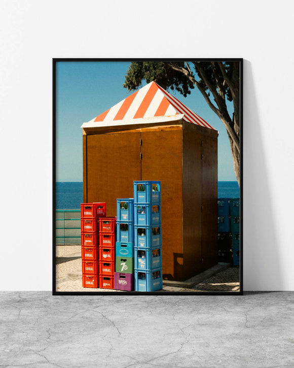 Colorful wall art of stacked red, blue and green vintage soda crates beside a striped seaside kiosk