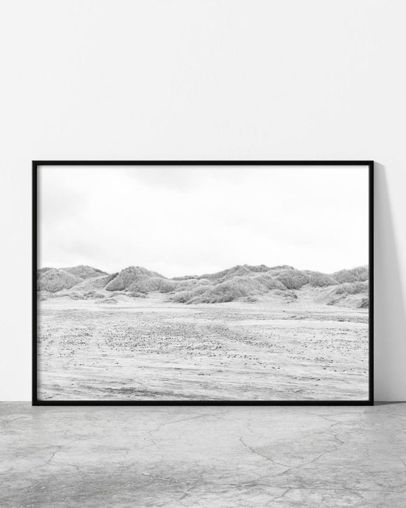 Black and white landscape photo of sand dunes with textured patterns under an overcast sky.