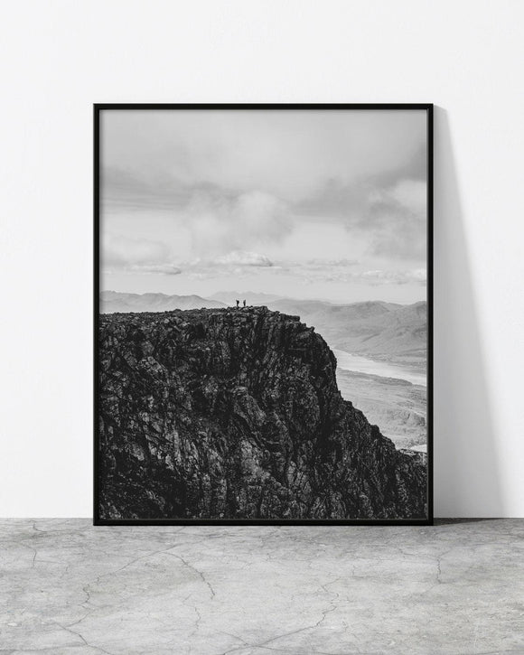 Black and white mountain landscape print featuring two hikers standing on a rugged cliff edge with vast scenery.