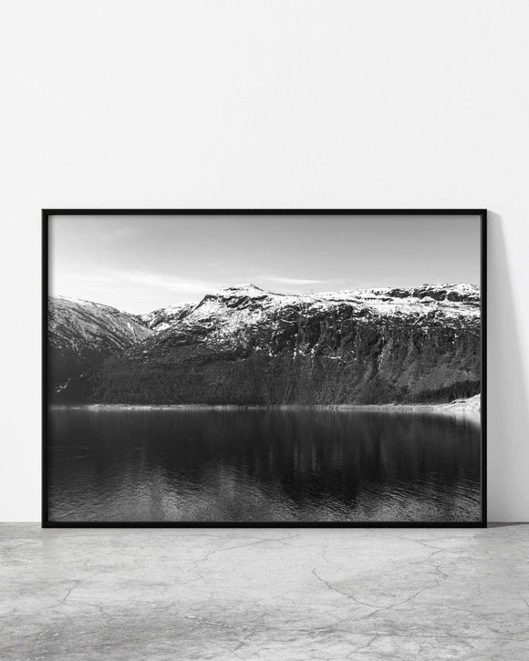 Black and white framed print of a serene mountain lake with rugged snow-capped peaks in the background