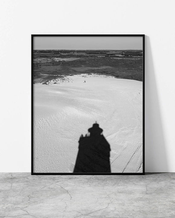 Black and white photo of a lighthouse shadow cast over a vast sandy landscape.