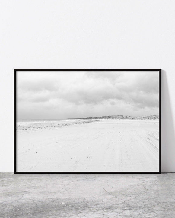 Minimalist black and white photo of a vast sandy beach under a cloudy sky.