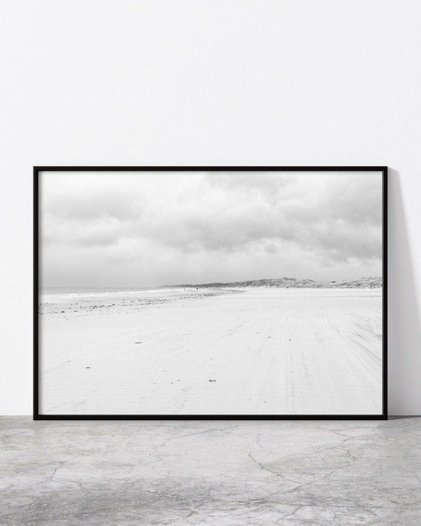 Minimalist black and white photo of a vast sandy beach under a cloudy sky.