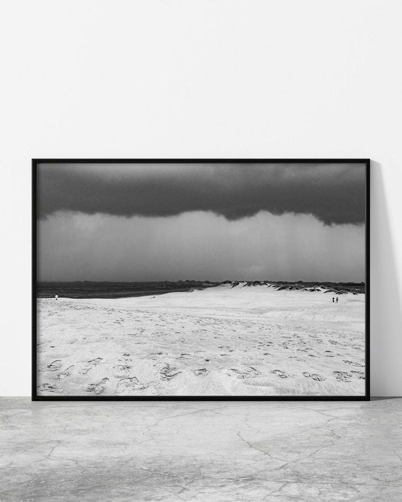 Monochrome desert scene with footprints scattered across soft dunes under a dark sky.