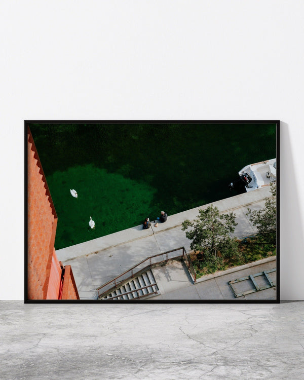 Stylish cityscape wall art featuring a waterside promenade with people, swans, and vibrant green water.