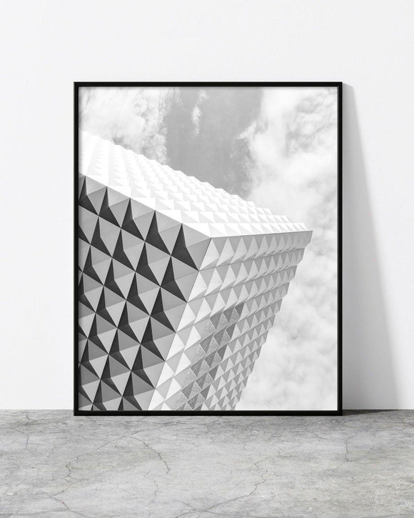 Black and white architectural photograph featuring a geometric building facade with triangular patterns against a cloudy sky.